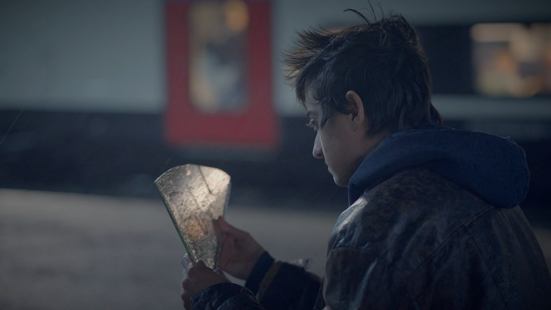 A young man sits on the floor at a train platform, staring at a shard of mirror with the word 'future' written on it. From the Mossbeard song - Failing at it