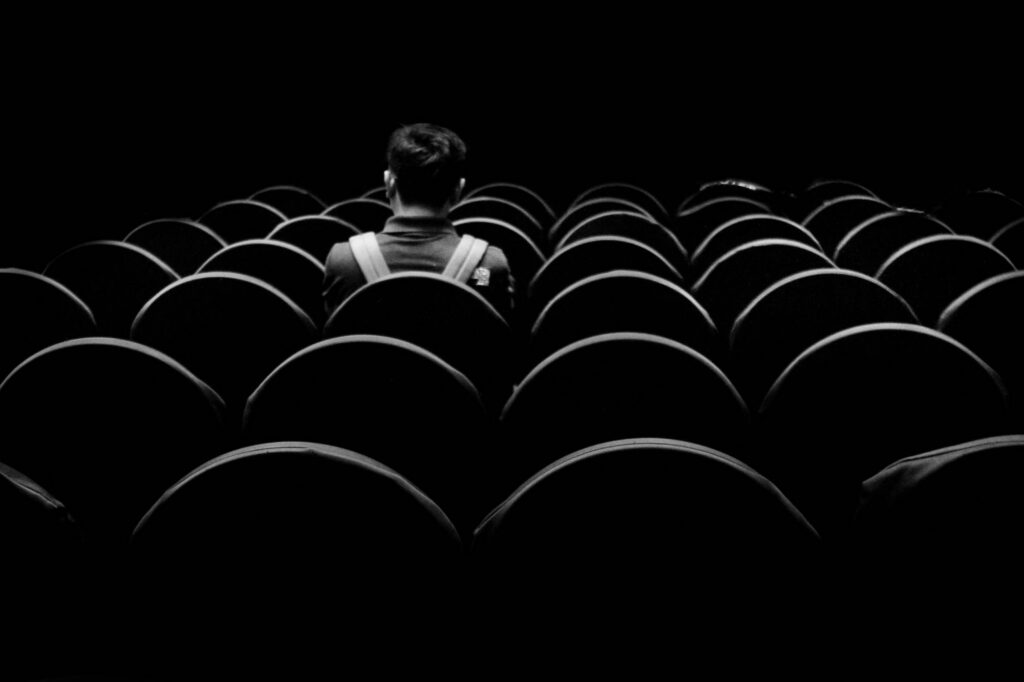 A rear view of a young man sitting alone in an auditorium. Black and white moody.