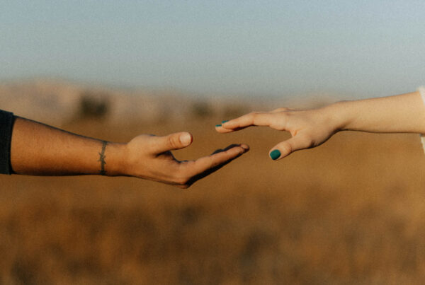 A man and a woman's hands reach for one another. They are of different races and are showing unity and love.