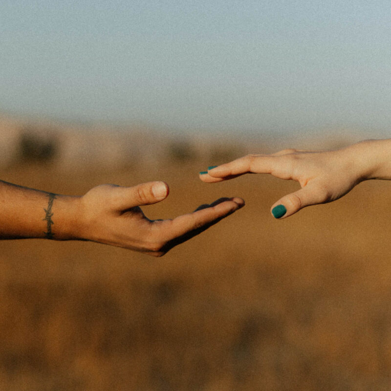 A man and a woman's hands reach for one another. They are of different races and are showing unity and love.