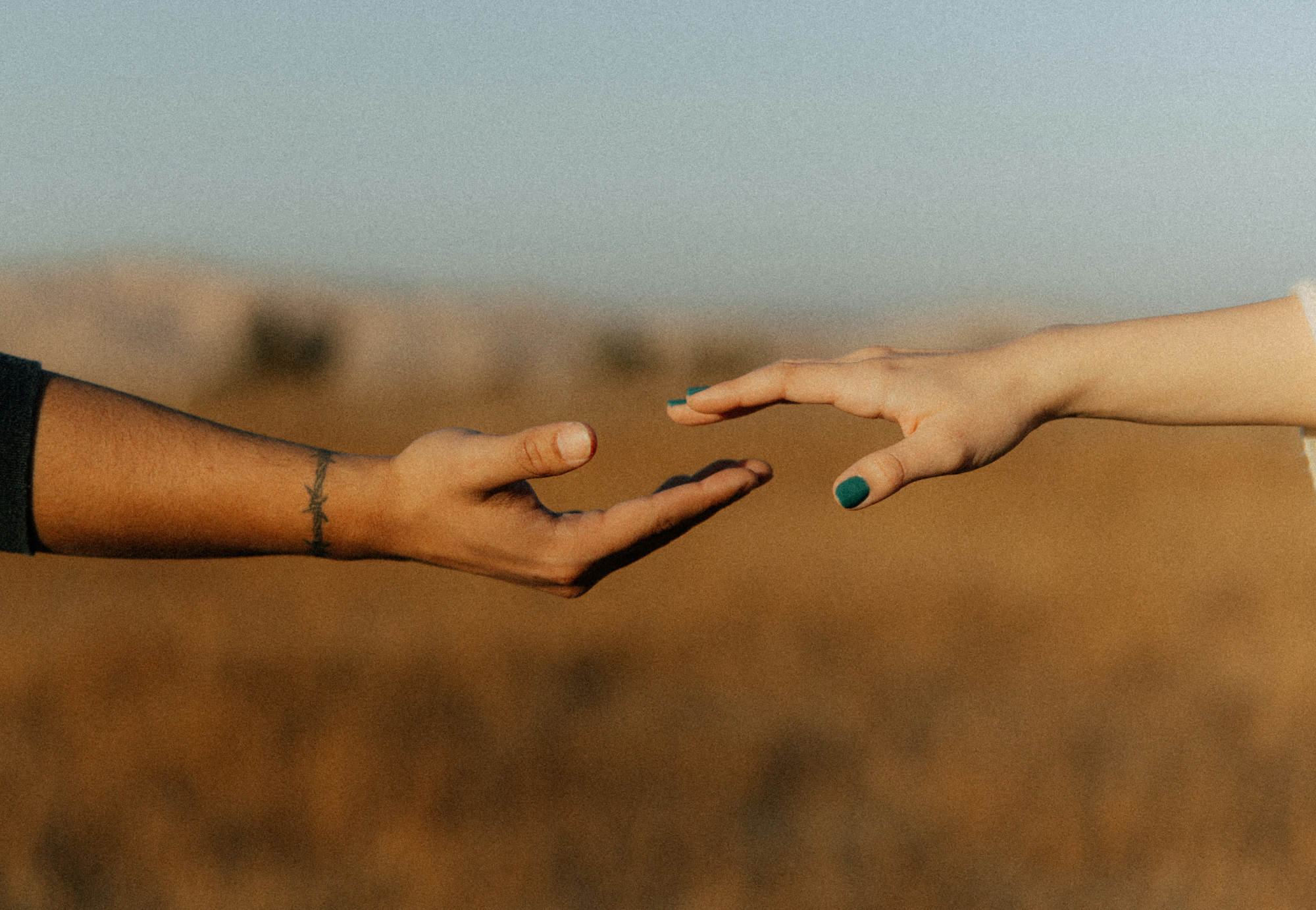 A man and a woman's hands reach for one another. They are of different races and are showing unity and love.