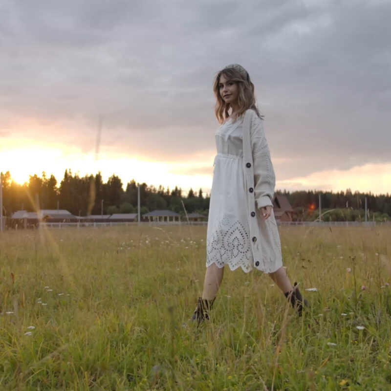 Mossbeard -Favourite mystery - A beautiful young woman wearing a white dress and boots, walks across a country field at sunset.