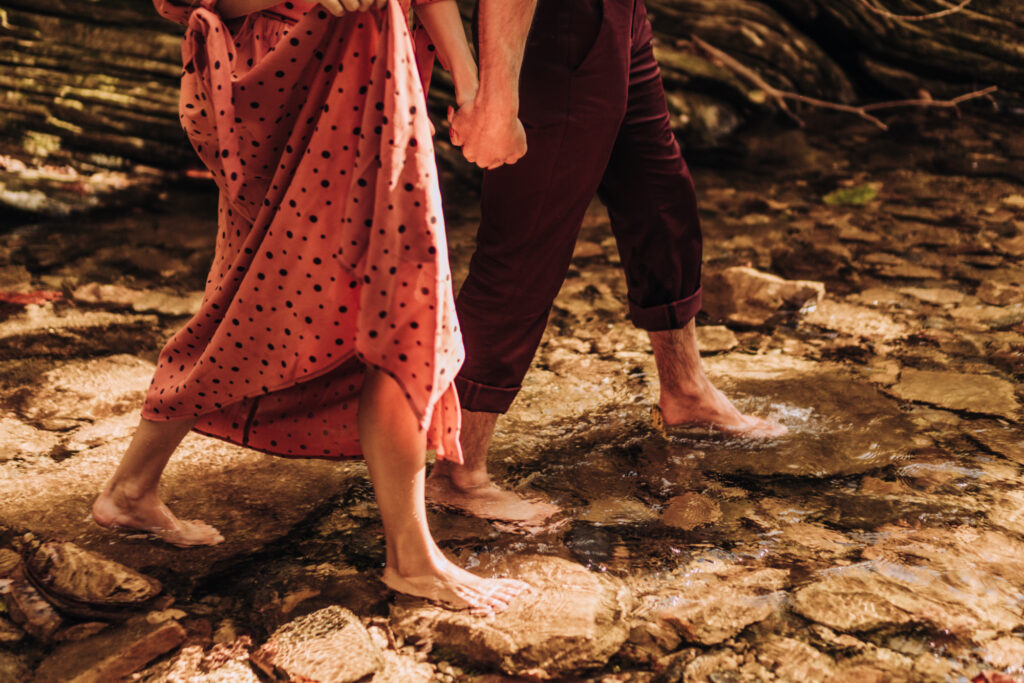 Mossbeard - Pathmaker - A man and a woman hold hands and walk bare footed through a shallow stream.