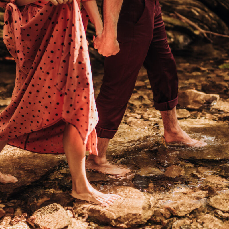 Mossbeard - Pathmaker - A man and a woman hold hands and walk bare footed through a shallow stream.