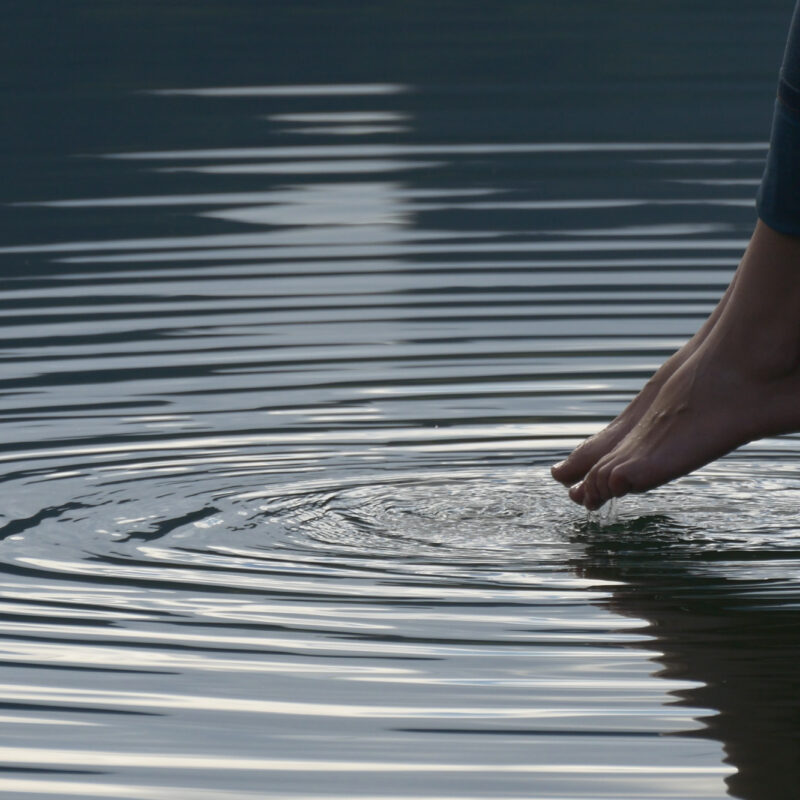 Mossbeard - The ripple - A close up of a woman's feet being dipped into a pond, creating a ripple.